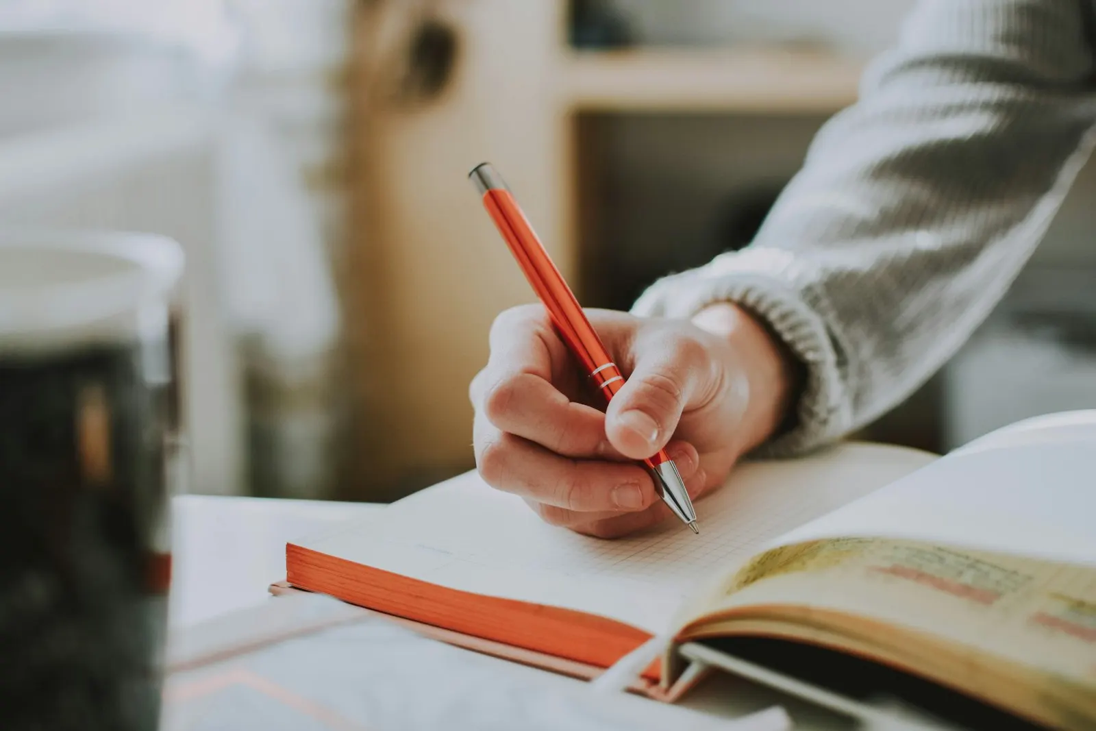 Une main tient un stylo rouge au-dessus d'un carnet ouvert