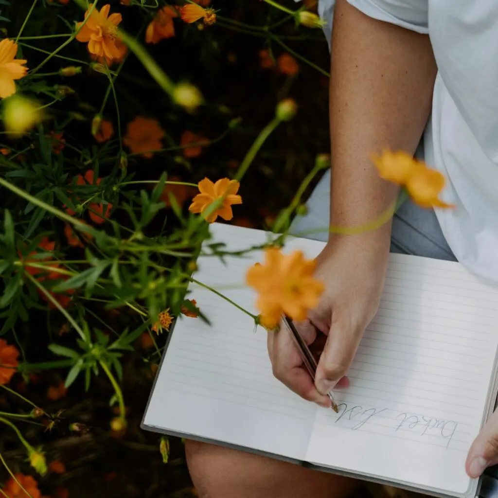 Personne écrivant dans un carnet au milieu de fleurs orange